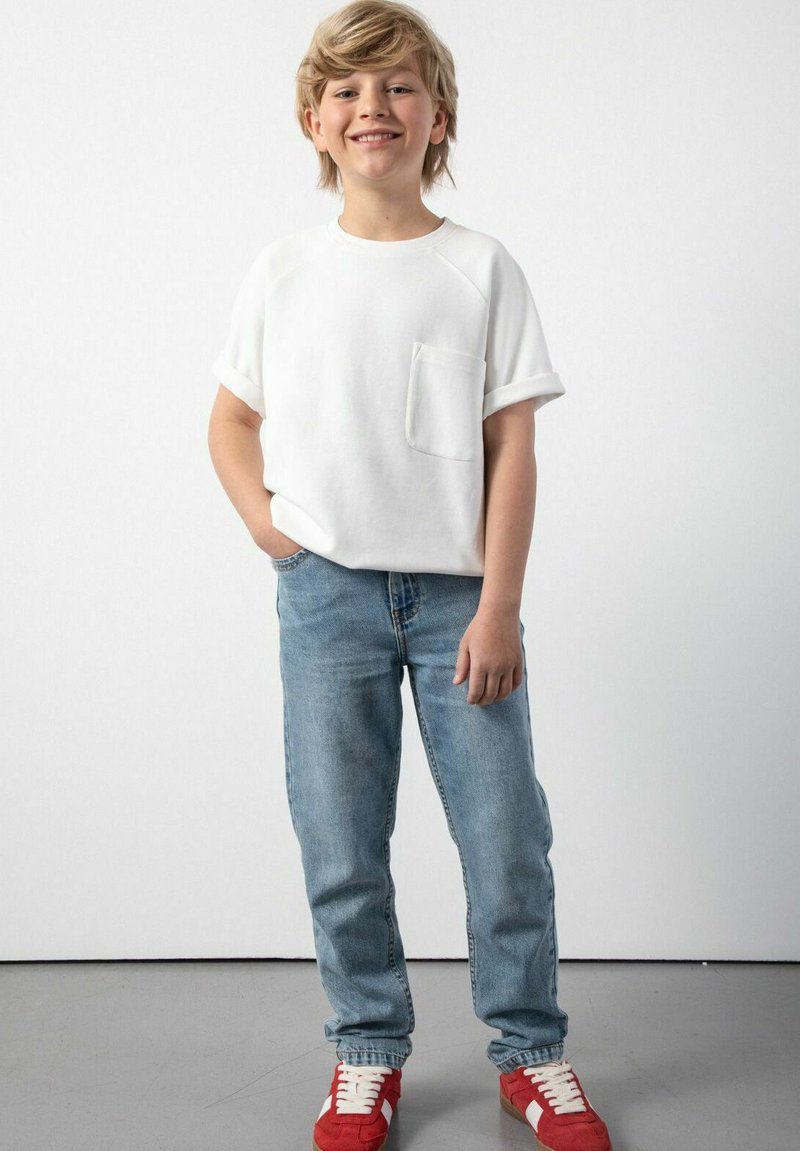 Biała koszulka z krótkim rękawem z kieszonką, w zestawie z jasnoniebieskimi dżinsami i czerwonymi trampkami. Stylizacja charakteryzuje się swobodnym, komfortowym wyglądem.