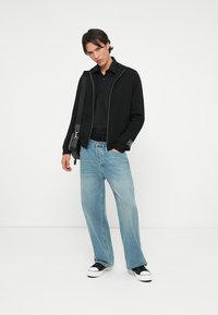 Black zip-up jacket with a smooth texture, black button-up shirt, light blue wide-leg jeans, and black sneakers with white soles.