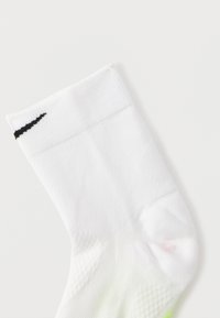 Άσπρη αθλητική κάλτσα με ριμπ υφή, που διαθέτει μαύρο λογότυπο Nike στη μανσέτα και διακριτική βαθμιδωτή πράσινη λεπτομέρεια στο δάχτυλο.