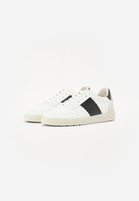 Sneakers bianchi con accenti neri, pelle liscia e pannelli testurizzati, design con lacci, punta tonda e suola in gomma ammortizzata.