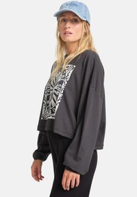 Schwarzer, kurzer Sweatshirt mit einem großen weißen grafischen Design auf der Vorderseite, langen Ärmeln mit elastischen Bündchen, kombiniert mit einer hellblauen Denim-Mütze.