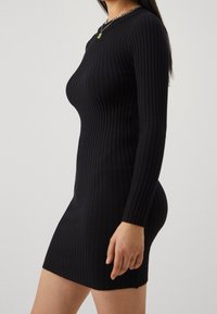 Svart blandad långärmad klänning med en figursydd passform, som når till mitten av låret. Har en rund halsringning och ett horisontellt ribbmönster över hela.