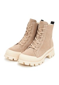 Beige suède enkellaarsjes met een stevige witte zool, voorzien van veters en een rits aan de zijkant voor gemakkelijk aantrekken. Textuur en naaddetails.