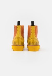 Botas tobilleras bicolor con parte superior de cuero texturizado naranja y suela de goma amarilla con tacos definidos y pestañas traseras para facilitar su puesta.
