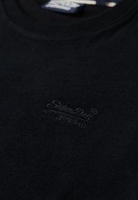 Sort bomulds t-shirt med rund hals og et subtilt broderet logo på forsiden. Glat tekstur, afslappet design, minimal detaljering.