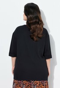 Camiseta negra de gran tamaño con mangas cortas enrolladas, presentada sobre un fondo blanco. Tela suave, diseño simple y un ajuste relajado.