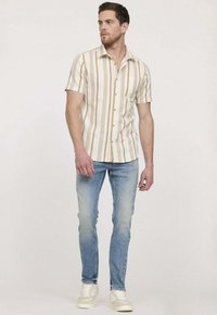 Chemise à manches courtes à boutons avec des rayures verticales en crème et beige. Associée à un jean skinny bleu clair et des baskets blanches.