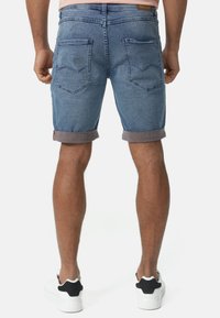 Shorts en denim bleu clair, avec des revers, des poches arrière avec des détails de couture, et un onglet en cuir sur la ceinture.