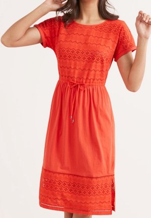 Robe en coton rouge à manches courtes, avec des motifs zigzag brodés et une taille à cordon. L'ourlet est orné de détails en œillets décoratifs.