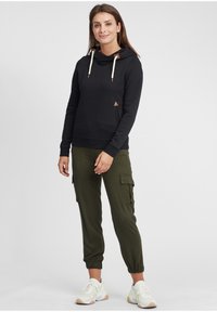 Felpa nera con collo a cascata e dettagli in pelle, abbinata a pantaloni cargo verde oliva con tasche laterali e polsi in elastico.