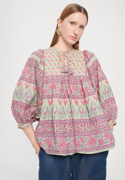 Floral-patterned blouse featuring pink and green hues, tie neck detail with tassels, and puffed sleeves. Soft fabric with a loose fit.