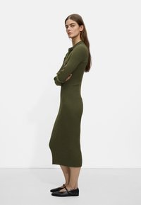 Ribbed dress dzianinowy w oliwkowym kolorze z długimi rękawami i dopasowanym krojem, w zestawieniu z czarnymi płaskimi butami z detalem w postaci paska.