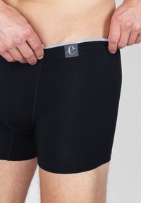 Zwarte katoenen boxershorts met een grijze elastische tailleband, met een logo-tag. De stof lijkt glad en heeft een strakke pasvorm.