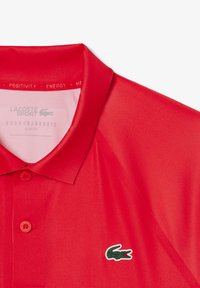 Röd Lacoste Sport polo i slim fit. Har en spetsig krage, treknapps manschett och en grön broderad logotyp på bröstet. Slät textur.