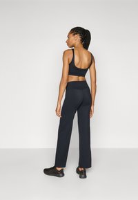 Zwarte sportieve crop top met brede banden, gecombineerd met hoge zwarte broeken, met een gladde textuur en een relaxte pasvorm.