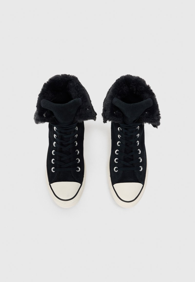 Schwarze High-Top-Sneaker aus Wildleder, mit einem flauschigen schwarzen Futter und einer weißen Gummikappe. Schnürsenkel und silberne Ösen sichtbar.