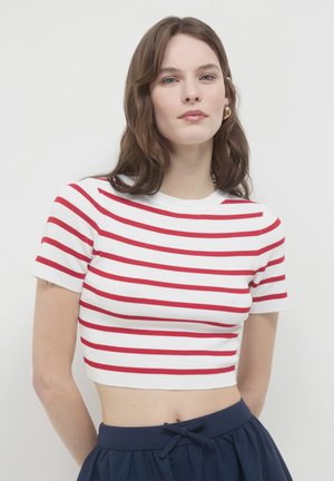Un crop top blanc à manches courtes avec des rayures horizontales rouges, texture côtelée et encolure ras du cou. Associé à une jupe bleu foncé avec un nœud.