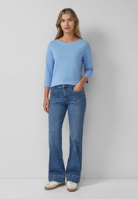 Light blue, long-sleeve top with a round neckline paired with straight-leg blue jeans featuring front pockets and a relaxed fit.