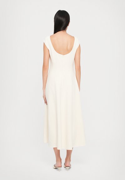 White, sleeveless dress with a deep scoop back, flowing A-line silhouette, and subtle texture. Fastened with a back zipper.