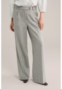 Grijze, visgraatpatroon wijde broek met plooien aan de voorkant, een knoopdetail in de taille en een gladde, gestructureerde stof. Gecombineerd met donkere schoenen.