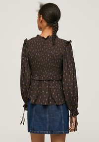 Blusa nera a fiori con corpetto arricciato, maniche lunghe a palloncino e dettagli in pizzo sul collo, abbinata a una gonna di denim.