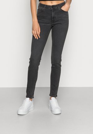 Jeans negros ajustados con cinco bolsillos, pasadores para cinturón y una textura ligeramente desgastada, combinados con zapatillas de plataforma blancas.
