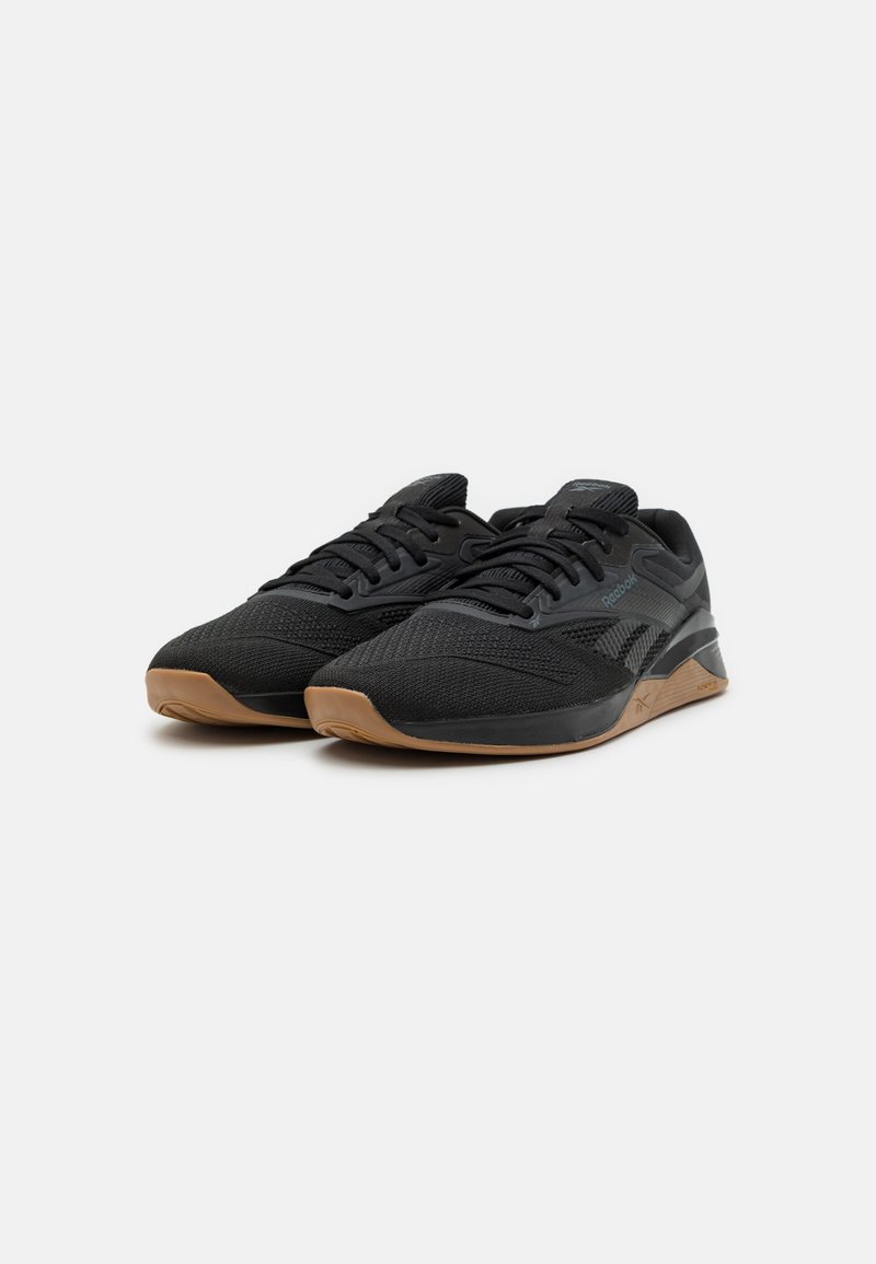 Baskets de sport noires avec une tige en maille texturée, des lacets plats et une semelle en gomme. Présente un design épuré avec une marque discrète.
