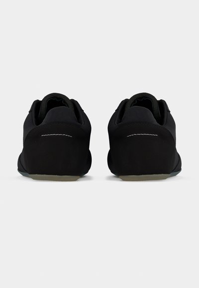 Ζευγάρι μαύρα sneakers χαμηλού ύψους, φωτογραφημένα από την πίσω πλευρά, με ελάχιστη ραφή και ανοιχτόχρωμες σόλες σε απλό φόντο.