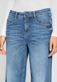 Light blue denim jeans with a straight leg design, five pockets, and a slightly faded texture. Button closure and brand label near the pocket.
