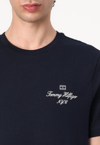 Navyblaue Baumwoll-T-Shirt mit Rundhalsausschnitt, mit weißem Logo-Text "Tommy Hilfiger N.Y.C." und einem kleinen Akzentgrafik.