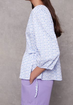 Blau-weiß kariertes Blusenshirt mit Puffärmeln und einer Schleife in der Taille, kombiniert mit einem lavendelfarbenen Unterteil. Strukturierter Baumwollstoff.