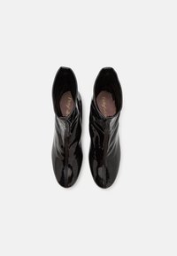 Botas de tobillo de charol negro con un acabado brillante, que cuentan con una cremallera frontal, punta redonda y textura suave.