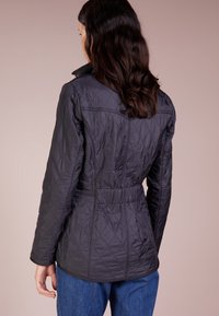 Prošívaná černá bunda s přiléhavým pasem, vysokým límcem a dlouhými rukávy. Obsahuje texturovaný design a jemné akcenty stehování.