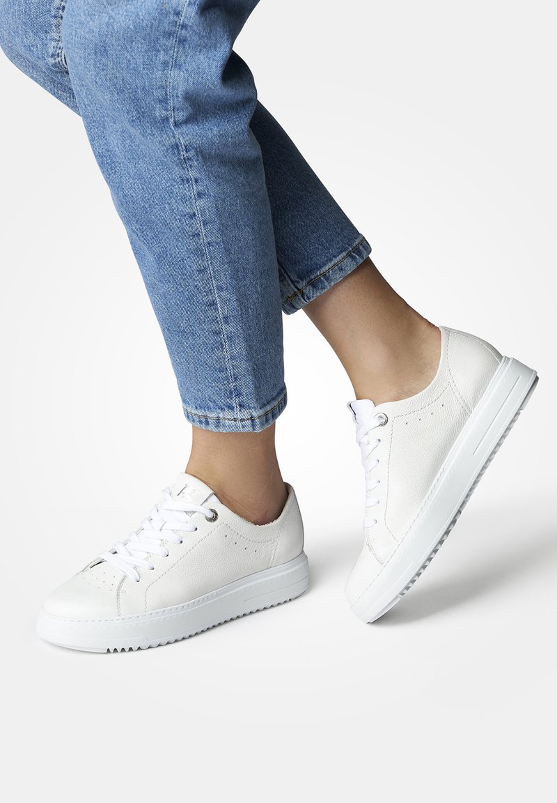 Baskets en cuir blanc avec une tige texturée, semelle en caoutchouc plate, bout arrondi et design à lacets, portées avec un jean en denim retroussé.