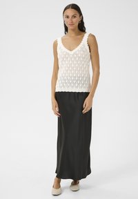 Lace gebreide mouwloze top in crème met een V-hals, gecombineerd met een lange, zwarte satijnen rok. Soepele textuur en ontwerp tot op de vloer.