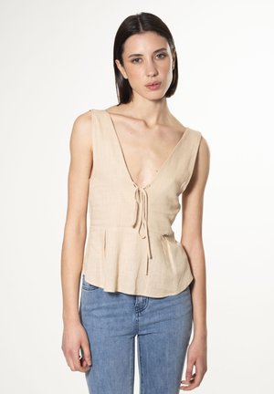 Top peplum in lino beige con scollatura a V profonda, dettaglio con nodo frontale e morbide pieghe. Presenta spalline larghe e un tessuto leggermente strutturato.
