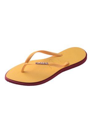 Żółto-bordowe gumowe japonki z teksturowaną podeszwą i pomarańczowymi paskami w kształcie litery Y z małym logo „Havaianas”.