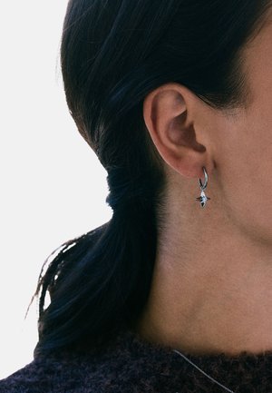 Sølv ørering med en lille stjernevedhæng. Øreringen er glat og skinnende, mens stjernevedhænget har en tekstureret overflade.