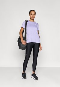 Violeta sporta krekls, melnas legingi un melnas sporta kurpes. Modelis tur tumši pelēku somu. Gluda tekstūra un piegulošs dizains.