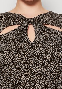 Top a fantasia nera e beige con dettagli a taglio e un nodo sul colletto; presenta un tessuto morbido e texturizzato.