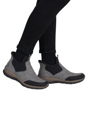 Gray ankle boots with black elastic side panels, textured black toe cap, and woven midsole. Smooth upper material with a sporty design.