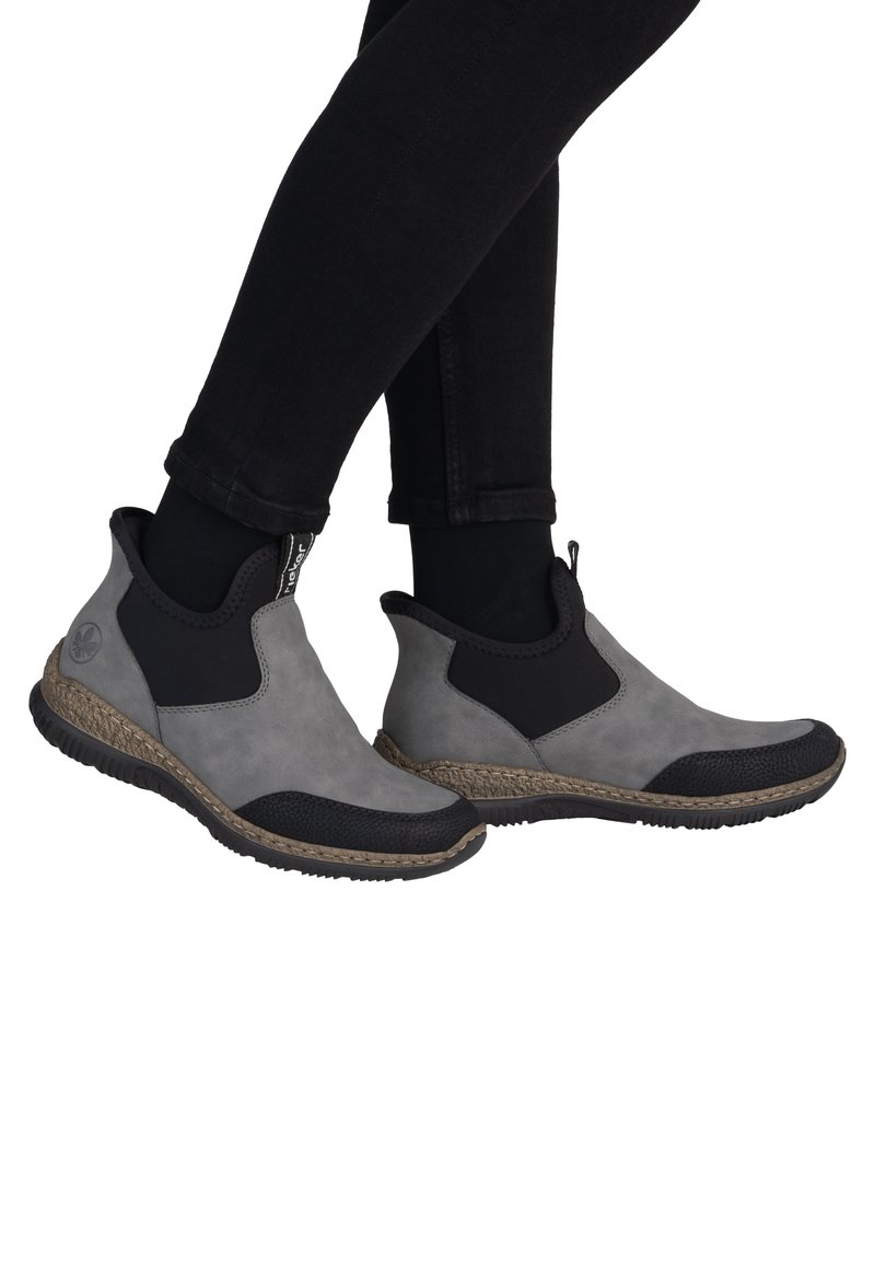 Bottines grises avec des panneaux élastiques latéraux noirs, un bout en cuir noir texturé et une semelle intermédiaire tissée. Matériau supérieur lisse avec un design sportif.