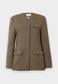 Blazer marrón a medida con cuello redondo, cierre frontal, un bolsillo en el pecho y dos bolsillos frontales con solapa. Tejido suave con líneas limpias.