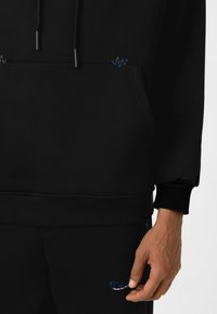 Zwarte hoodie met een buidelzak, verstelbare trekkoord en contrasterende blauw-grijze golfpatroon borduring op de borst.