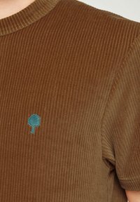 Bruine corduroy t-shirt met ribbeltextuur, voorzien van een teal boomembleem op de borst en een klassieke ronde hals.
