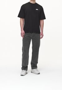 Camiseta de algodón negra de manga corta con un logo en el pecho, combinada con unos jeans de mezclilla rectos en color gris y zapatillas deportivas blancas.