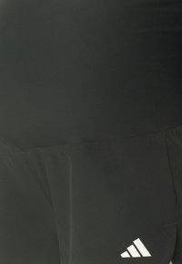 Gros plan d'un tissu noir avec un petit logo Adidas blanc sur la partie inférieure droite, montrant les détails de couture et de texture.