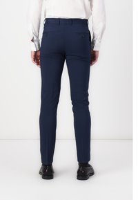 Marineblau, schmal geschnittene Hose mit glatter Textur, ausgestattet mit zwei Gesäßtaschen und einem Gürtelschlaufenbund, kombiniert mit schwarzen Schuhen.
