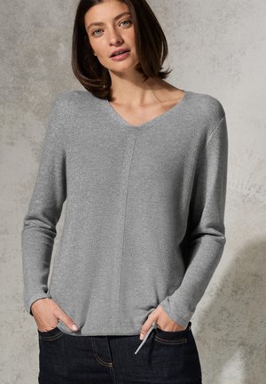 Grå v-ringad tröja med långa ärmar och en texturerad stickdesign. Har en subtil lyster och en avslappnad passform. Tillsammans med mörka denimjeans.