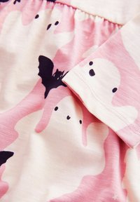 Tissu rose pâle avec un motif de fantômes blancs et de chauves-souris noires. Texture lisse avec taille froncée et manches courtes. Design décontracté.